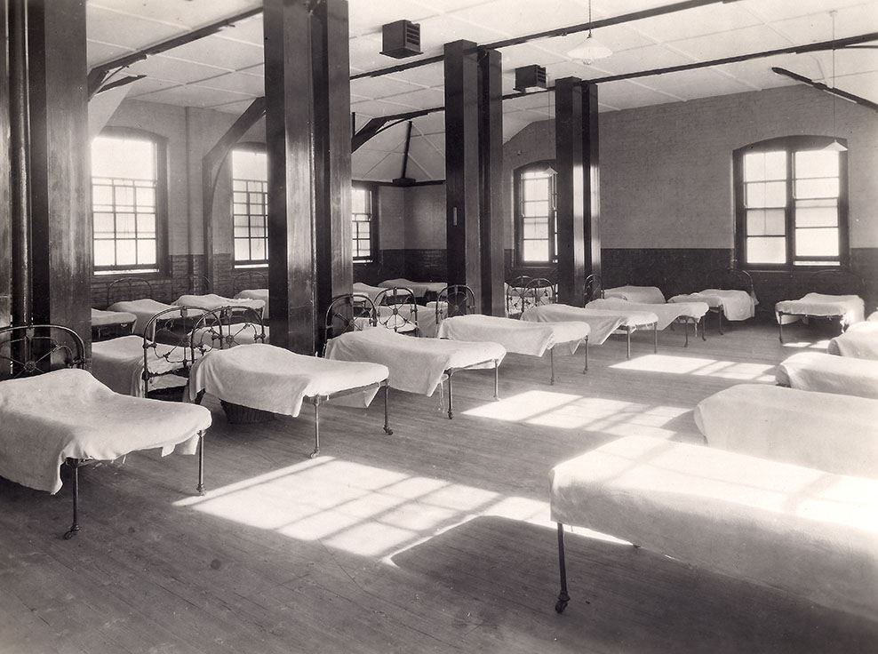 A black and white picture of a ward in the Foundling Hospital, Redhill. Multiple beds are lined uniformly in rows all of them have the same white sheets.