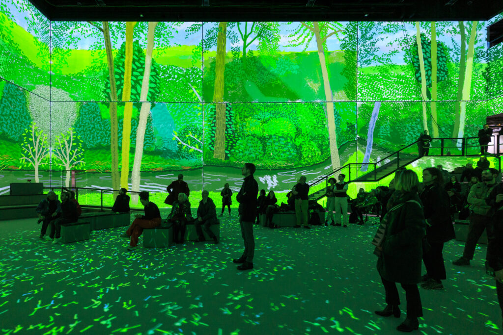 Visitors at the digital Hockney exhibition silhouetted against a vibrant green background