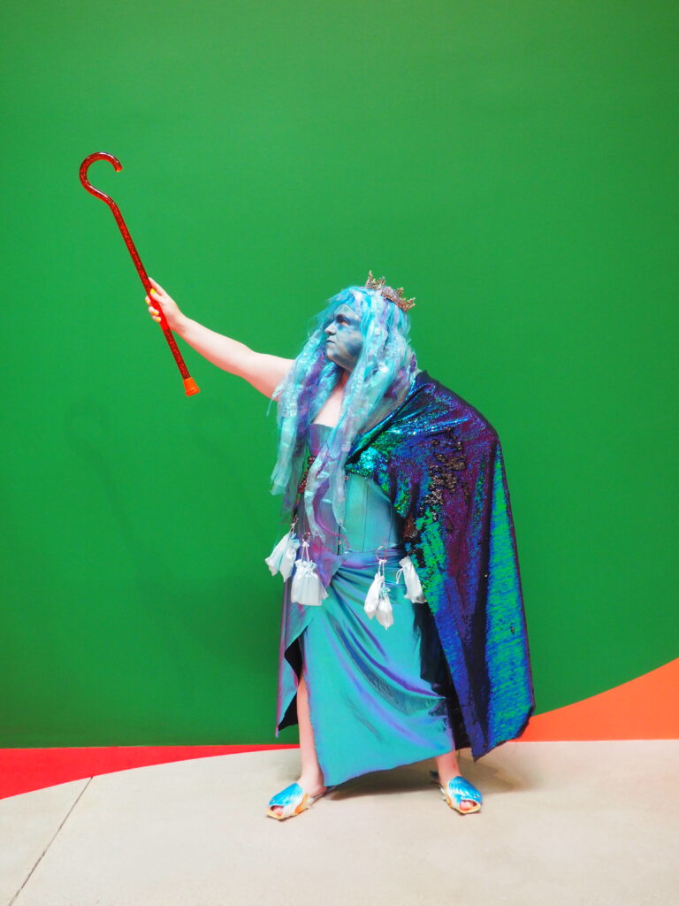 A person dressed in a blue costume and holding aloft a walking stick