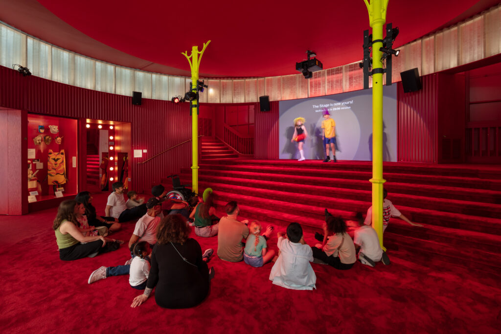 Red carpeted space made to look like a theatre with children watching a projection 